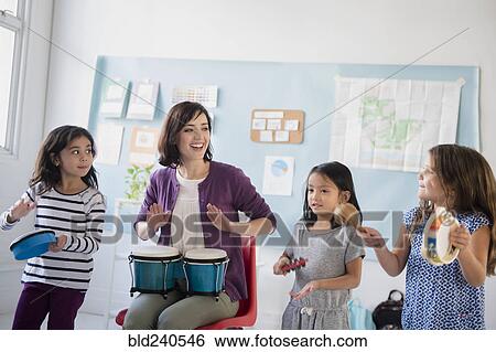 Stock Photograph - Teacher and girls playing bongos and tambourines in classroom. Fotosearch