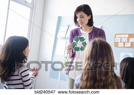 Stock Photo - Teacher showing recycling symbol to girls in classroom. Fotosearch
