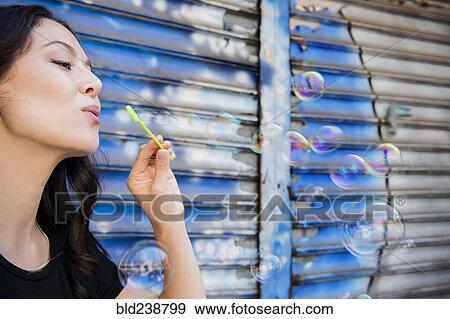 Stock Photo - Thai woman blowing bubbles in city. Fotosearch
