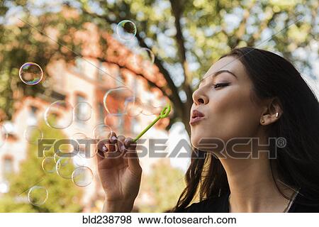 Stock Photo - Thai woman blowing bubbles in park. Fotosearch