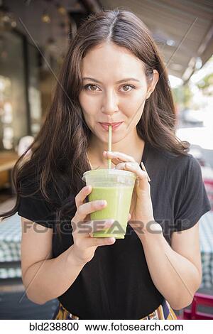 Stock Image - Thai woman drinking green smoothie. Fotosearch