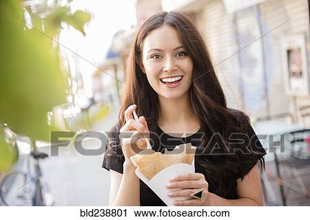 Stock Image - Thai woman eating food in city. Fotosearch