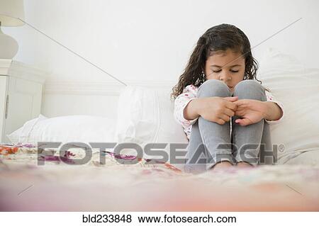 Stock Photo - Unhappy Mixed Race girl sitting on bed. Fotosearch
