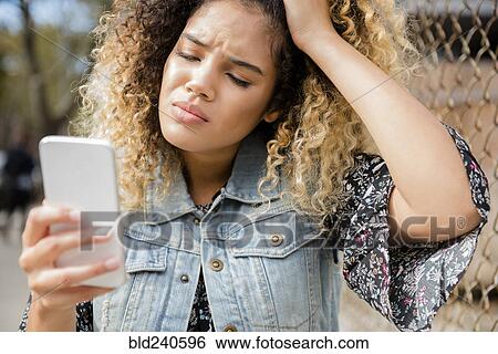 Stock Photograph - Unhappy Mixed Race woman texting on cell phone. Fotosearch