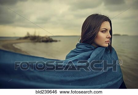 Stock Photograph - Wind blowing blue blanket of Caucasian woman at beach. Fotosearch