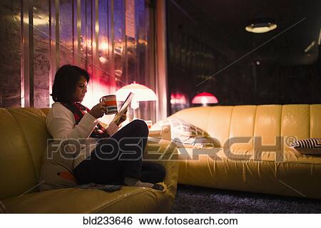 Woman drinking tea and reading magazine on sofa View Large Photo Image Stock Photograph - Woman drinking tea and reading magazine on sofa. Fotosearch