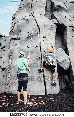 Stock Photography - Woman holding rope for man climbing rock climbing wall. Fotosearch