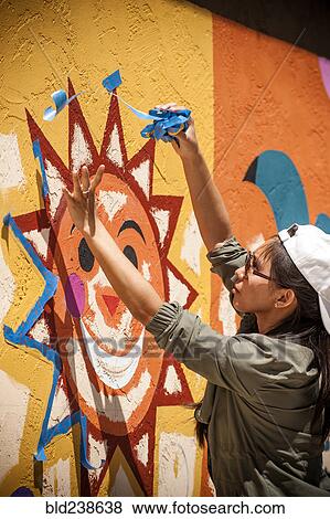 Stock Photo - Woman removing painting tape from mural on wall. Fotosearch
