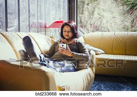 Stock Photo - Woman sitting on sofa texting on cell phone. Fotosearch
