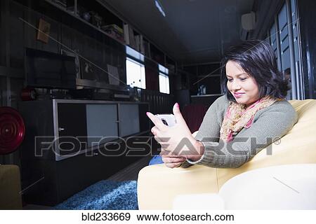 Stock Photo - Woman sitting on sofa texting on cell phone. Fotosearch
