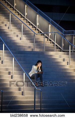 Stock Photo - Woman sitting on staircase texting on cell phone. Fotosearch