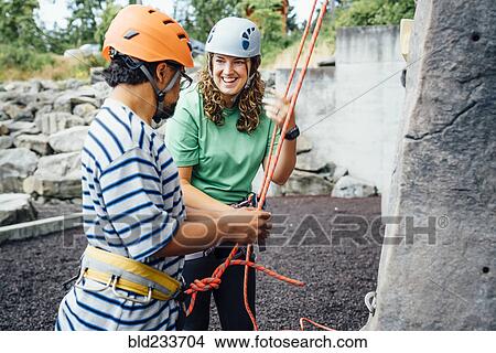 Picture - Woman smiling to man preparing to climb rock climbing wall. Fotosearch
