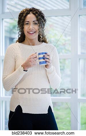 Woman standing near window holding coffee cup View Large Photo Image Stock Image - Woman standing near window holding coffee cup. Fotosearch