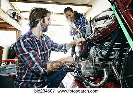 Stock Photo - Woman watching man repairing motorcycle in garage. Fotosearch