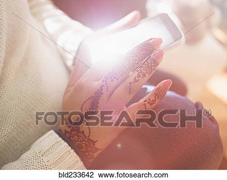 Stock Image - Woman with henna tattoos on hands texting on cell phone. Fotosearch