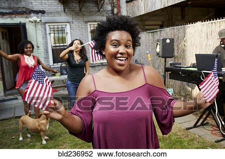 Stock Image - Women celebrating with American flags in backyard. Fotosearch