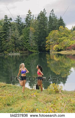 Stock Photograph - Women stretching legs near lake. Fotosearch