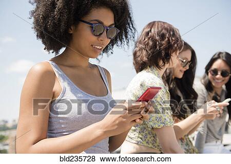 Women texting on cell phones outdoors View Large Photo Image Stock Photo - Women texting on cell phones outdoors. Fotosearch