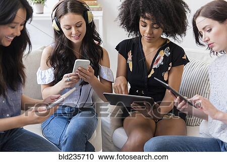 Stock Image - Women using technology in livingroom. Fotosearch