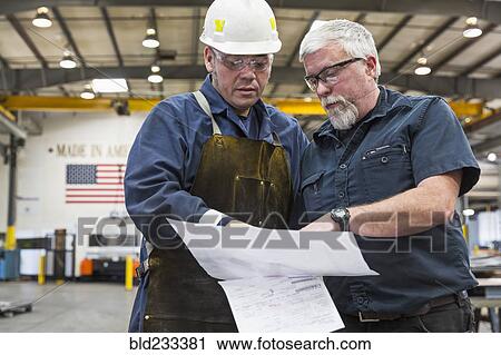 Workers reading paperwork in factory View Large Photo Image Stock Image - Workers reading paperwork in factory. Fotosearch