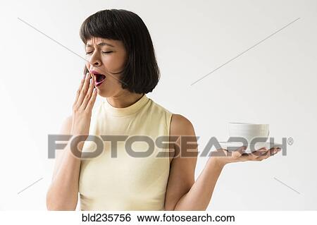 Stock Photograph - Yawning Hispanic woman holding coffee cup. Fotosearch