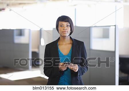 Stock Photography - African American businesswoman holding cell phone in office. Fotosearch