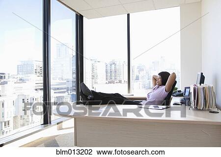 Stock Image - African American businesswoman sitting at desk with feet up. Fotosearch