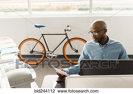 Stock Image - African American man reading paperwork in office. Fotosearch