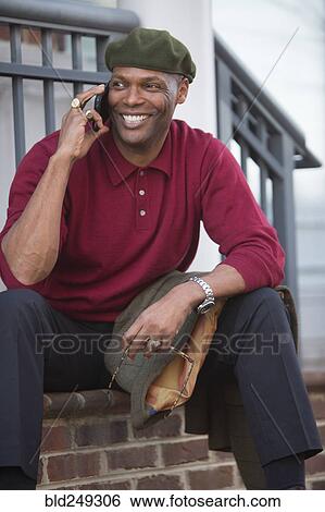 Stock Photograph - African American man sitting on stoop talking on cell phone. Fotosearch