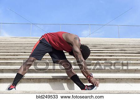 Stock Image - African American man stretching leg on bleachers. Fotosearch
