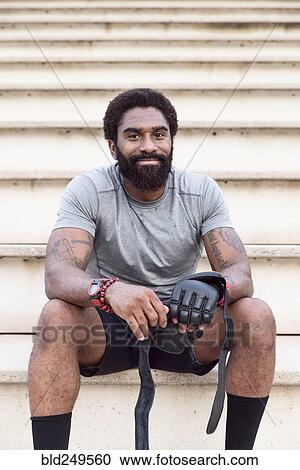 Stock Image - African American men sitting on bleachers unwrapping boxing gloves. Fotosearch