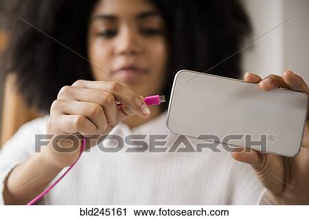 Stock Image - African American woman connecting cable to cell phone. Fotosearch