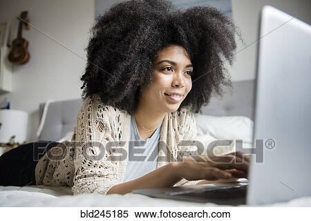 Stock Photography - African American woman laying in bed using laptop. Fotosearch