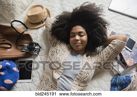Stock Image - African American woman laying on bed anticipating travel. Fotosearch