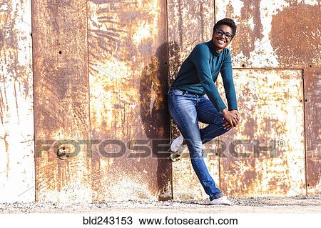 Stock Image - African American woman leaning on rusty metal wall. Fotosearch