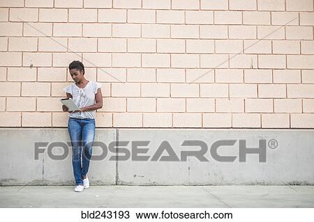 Stock Image - African American woman leaning on concrete wall using digital tablet. Fotosearch
