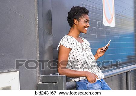 Stock Photo - African American woman leaning on railing texting on cell phone. Fotosearch