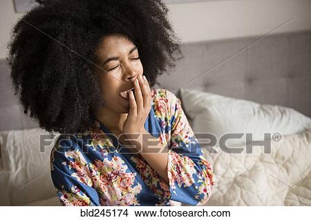 Picture - African American woman sitting in bed and yawning. Fotosearch