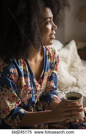 Stock Photography - African American woman sitting in bed drinking coffee. Fotosearch