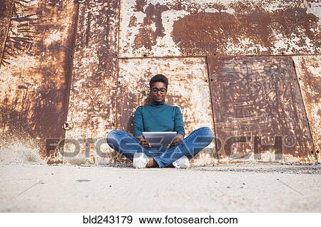 Stock Photo - African American woman sitting on ground using digital tablet. Fotosearch
