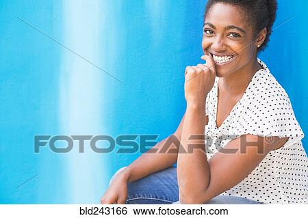 Stock Photograph - African American woman smiling near blue wall. Fotosearch