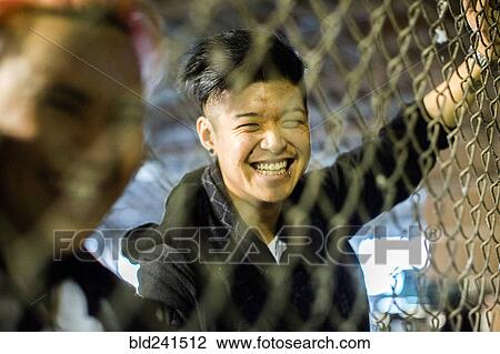 Stock Image - Androgynous Asian man and woman leaning on fence. Fotosearch
