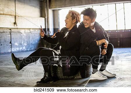 Stock Photo - Androgynous Asian man and woman posing for cell phone selfie. Fotosearch