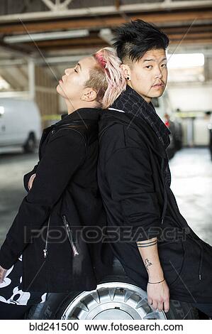 Stock Image - Androgynous Asian man and woman sitting on wheel. Fotosearch