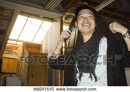 Stock Image - Androgynous Asian man holding scarf on head. Fotosearch