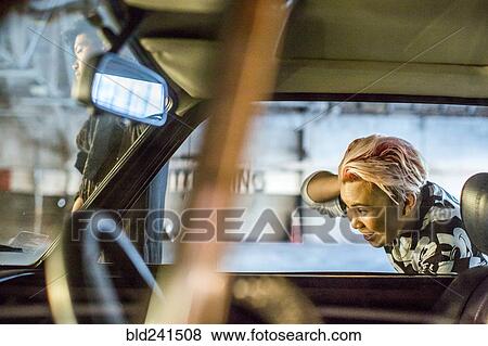 Stock Photo - Androgynous Asian woman checking hair in side-view mirror. Fotosearch