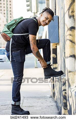 Stock Image - Androgynous Mixed Race woman carrying backpack adjusting boot. Fotosearch