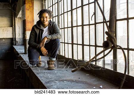 Stock Image - Androgynous Mixed Race woman smiling near window. Fotosearch