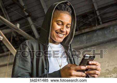 Stock Photography - Androgynous Mixed Race woman texting on cell phone. Fotosearch