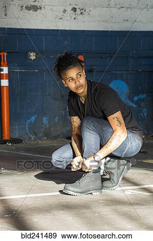 Stock Photo - Androgynous Mixed Race woman tying shoelace. Fotosearch
